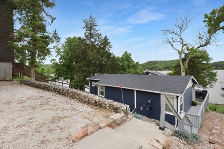 Charming lakeside retreat nestled among mature trees with scenic water views and easy access. The property sits on a hillside with a paved driveway and private parking.