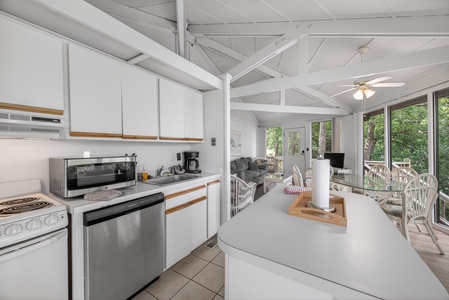 Your bright, fully-equipped kitchen flows into a cozy living space framed by large windows overlooking lush greenery, perfect for preparing meals while staying connected to nature.