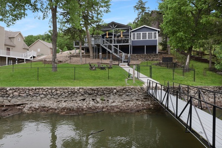 Charming lakefront property featuring a private dock and spacious waterfront lawn, nestled in a peaceful residential area surrounded by mature trees and neighboring homes.