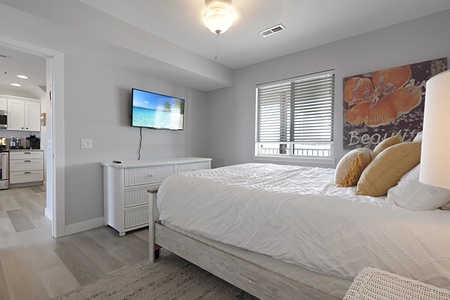 Unwind in your peaceful bedroom featuring a comfortable bed, wall-mounted TV, and bright natural light filtering through stylish blinds.