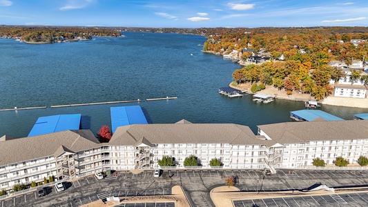 Aerial view of lakefront property complex with scenic lake surrounded by vibrant autumn foliage and residential neighborhoods.