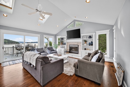 Sink into plush sofas and savor sweeping water views through floor-to-ceiling windows. Your peaceful lakeside retreat features a cozy fireplace, vaulted ceilings, and direct deck access for morning coffee or evening relaxation.