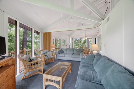 Unwind in your light-filled living room, where floor-to-ceiling windows frame lush forest views and cozy coastal furniture invites you to relax after a day of exploration.