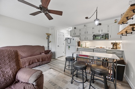 Your cozy retreat features a full kitchen with modern appliances, a comfortable living area with ceiling fan, and a breakfast bar perfect for morning coffee or casual meals together.