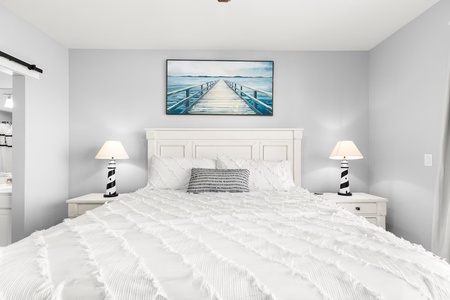 Sink into crisp white linens in your serene bedroom, where coastal artwork and lighthouse-themed lamps create a peaceful seaside retreat.