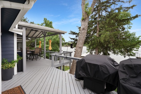 A beautifully designed outdoor deck perfect for relaxing mornings and evenings, complete with covered dining space and pristine lake views framed by mature trees.