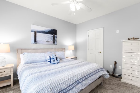 Unwind in your serene bedroom featuring coastal blue linens, soft lighting, and peaceful lake artwork creating your perfect retreat.