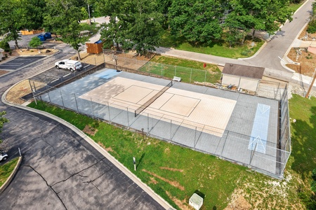 Aerial view of the property's multi-sport court set within a tree-lined residential neighborhood, featuring dedicated spaces for basketball, tennis, and pickleball activities surrounded by fenced perimeter.