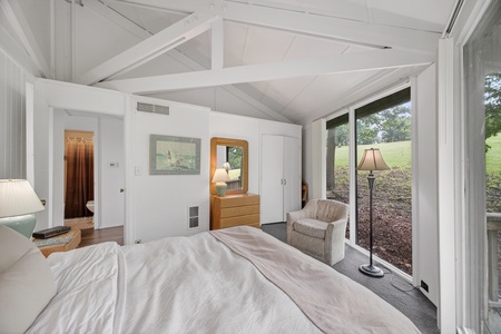 Unwind in your serene bedroom retreat where vaulted ceilings create an airy ambiance and large windows invite natural light to dance across crisp linens, making every morning feel like a peaceful escape.