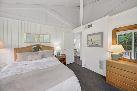 Sink into fresh linens and coastal charm. Your serene bedroom overlooks lush greenery through bright windows, while soft lighting and beachy decor create a peaceful retreat for restful nights.