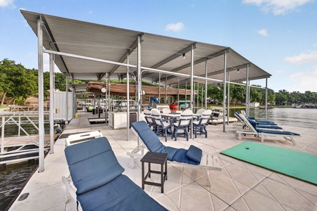 This spacious waterfront dock features lounge chairs, outdoor dining, and a grill under a shaded canopy—your perfect spot to relax by the lake, enjoy meals outdoors, and soak in serene water views.
