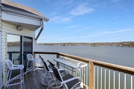 Waterfront deck with seating overlooking a scenic lake and residential shoreline community.