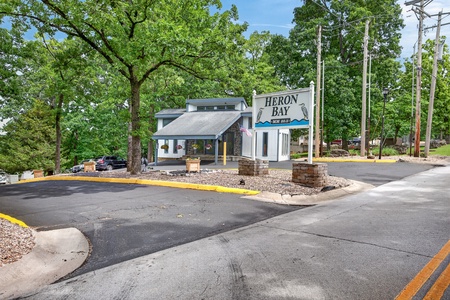 The entrance to Heron Bay at the Lake, featuring a covered parking area and property signage surrounded by mature trees.