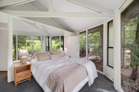Wake up surrounded by nature in this serene bedroom where sunlight filters through floor-to-ceiling windows on three sides, bringing the peaceful forest landscape right to your bedside for an unforgettable escape.