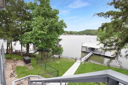 Peaceful waterfront property with private dock access on a calm lake, surrounded by mature trees and rolling hills in the distance.