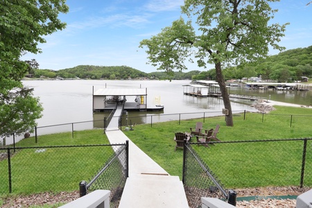 Private waterfront path leads to covered boat dock and lakeside fire pit, with tree-shaded lawn and rolling hills creating a serene waterside escape.