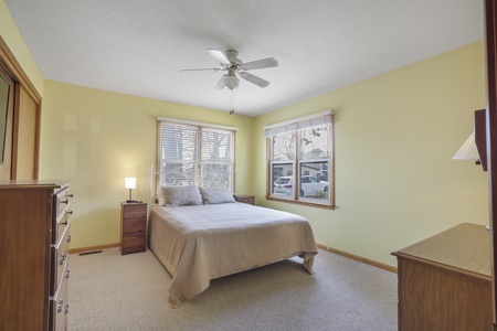 Unwind in your peaceful bedroom featuring cheerful yellow walls, plush bedding, and natural light streaming through dual windows.