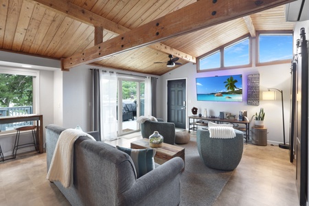Unwind in your spacious living room with soaring wood beam ceilings, cozy seating, and natural light pouring in through floor-to-ceiling windows overlooking the outdoor deck.