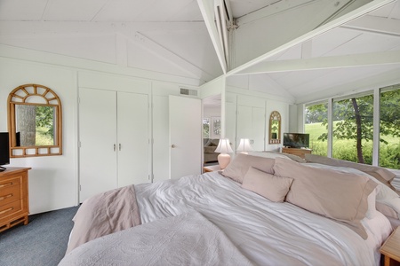 Wake up to peaceful pastoral views through sweeping windows that frame lush greenery and open fields. The vaulted ceiling creates an airy, open feeling above your restful space.