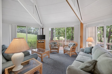 You'll love unwinding in this bright, vaulted living space—soft sofas, warm lighting, and floor-to-ceiling windows framing lush greens and your private deck. Picture peaceful mornings here.