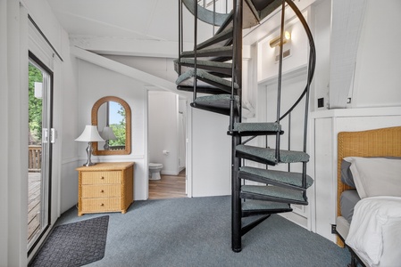 Curl up in your cozy bedroom retreat with a charming spiral staircase leading to a private loft above, while natural light pours in through large windows overlooking lush greenery.