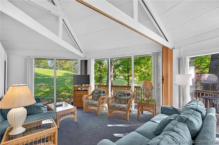 Relax in your bright living space where expansive windows frame lush green views and vaulted ceilings create an airy, open feel—perfect for peaceful mornings or cozy evenings together.