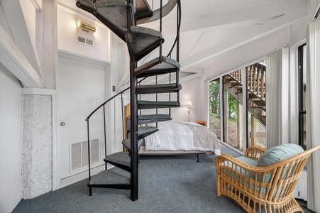Unwind in your cozy bedroom featuring a dramatic spiral staircase, plush bed, and serene garden views through tall windows that flood the space with natural light.