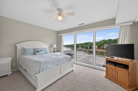 Wake up to serene lake views from your comfortable bedroom, where floor-to-ceiling windows frame peaceful waterfront scenery and gentle breezes from the ceiling fan enhance your restful retreat.