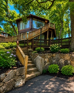 A tree-shaded retreat perched among lush greenery, where stone pathways and blooming hydrangeas lead to your elevated escape with wraparound decks and abundant natural light.
