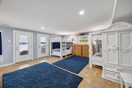 Your spacious bunk room offers plenty of sleeping spots with charming white bunk beds, soft blue rugs underfoot, and private outdoor access through French doors. Perfect for kids or groups who want their own space to unwind together.