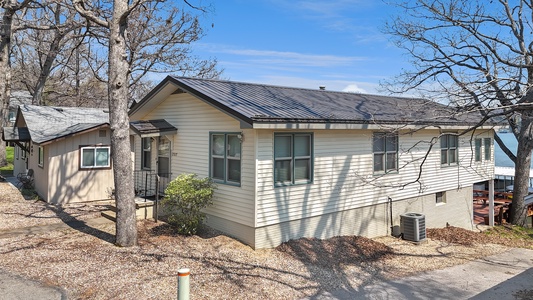 Charming lake house with modern metal roofing, surrounded by mature trees in a peaceful residential setting.