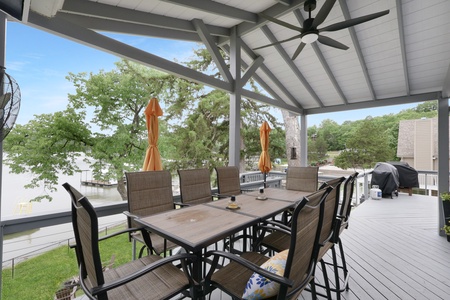 Spacious covered deck with lakefront dining for ten, complete with ceiling fan and BBQ grill. Perfect for outdoor meals with serene water views and mature oak trees.