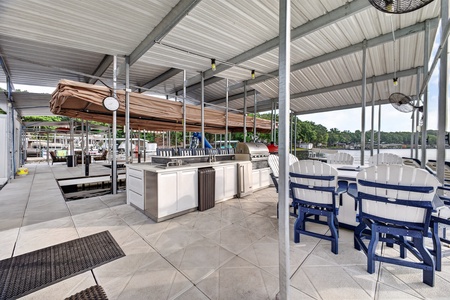 A covered waterfront entertaining space features a built-in outdoor kitchen with stainless steel appliances and comfortable dining areas overlooking the marina. Perfect for gatherings with stunning water views.