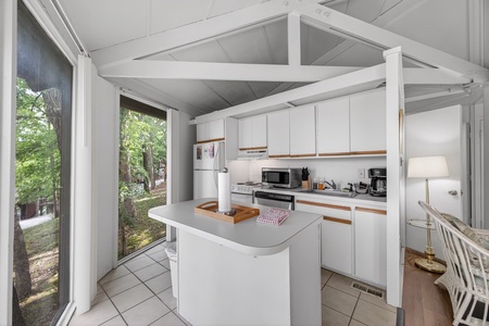 Your bright kitchen invites you to prepare meals with nature views through large glass doors that frame the surrounding trees and garden.
