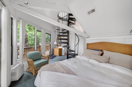 Step into your bright, airy bedroom where a stunning spiral staircase adds architectural charm and plush bedding invites restful nights. Your private deck awaits just beyond the glass doors, framed by trees.