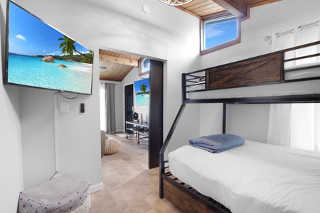 Your cozy space features a bunk bed with soft linens, a large TV for entertainment, and wood-accented high ceilings that add warmth and character to the room.
