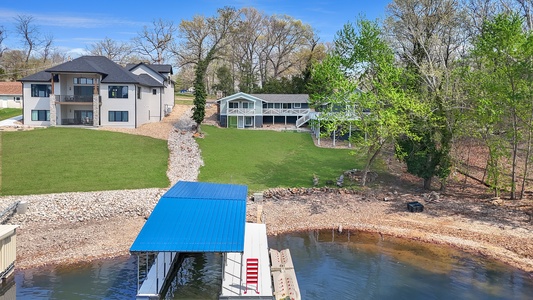 Lakefront property featuring modern home with private dock and boat house, surrounded by mature trees and manicured grounds.