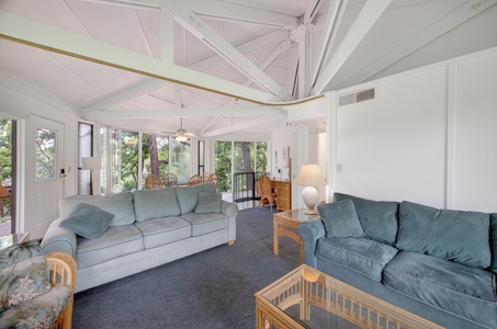 Relax in your spacious living room with soaring vaulted ceilings and abundant natural light streaming through large windows overlooking lush greenery.