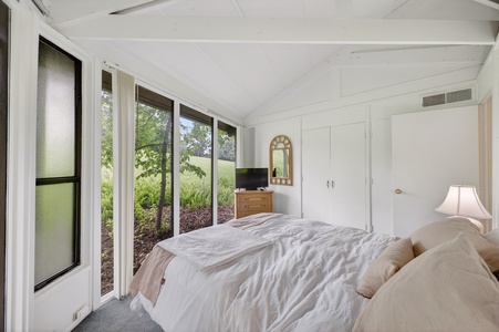 Wake up to a peaceful garden view from your cozy bedroom, complete with comfortable bedding, ample storage, and serene natural light flooding through expansive windows.