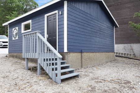 A charming blue cottage with white trim and a welcoming entrance staircase, marking your arrival at this cozy vacation retreat.