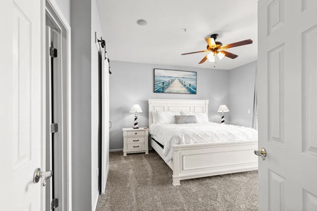 Your serene bedroom retreat awaits with crisp white linens, coastal artwork, and a ceiling fan for perfect comfort.