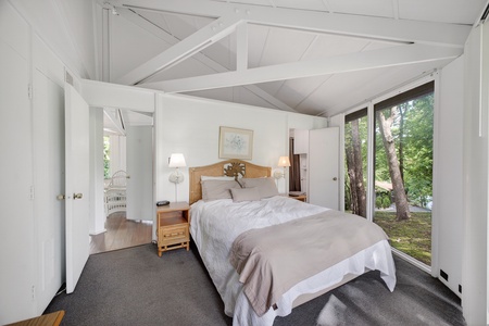 Wake up to sunlit trees framing your peaceful retreat. This bright bedroom features vaulted ceilings, cozy bedding, and a serene forest view to make your mornings unforgettable.