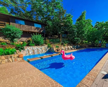 A modern vacation retreat nestled among lush greenery, featuring a sparkling pool with stone accents under a brilliant blue sky—your perfect sunny escape awaits.
