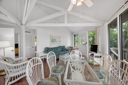 Your sunlit sanctuary showcases soaring vaulted ceilings with charming exposed beams, cozy seating, and large windows framing lush forest views—perfect for unwinding in peaceful elegance.