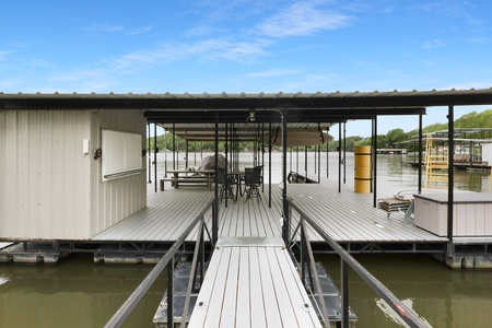 Covered boat dock with outdoor dining area situated on calm lake waters, offering direct waterfront access and scenic surroundings for peaceful lakeside relaxation.