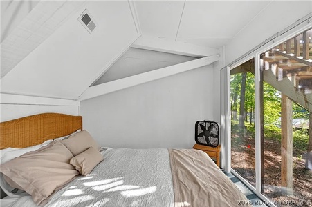 Sunlight filters through floor-to-ceiling windows framing forest views as you wake up in this serene loft bedroom with soaring vaulted ceilings.