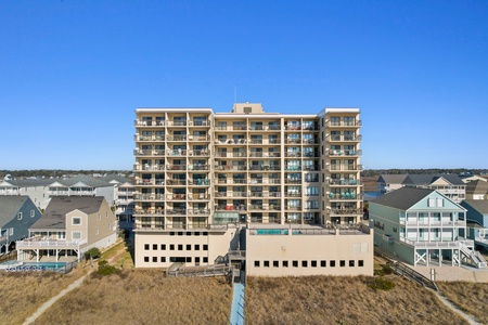 Modern beachfront condominium complex featuring multiple balconies and surrounded by coastal vacation homes in a peaceful residential area.