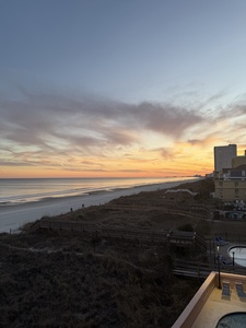 A stunning golden sunset paints the sky over this coastal location, with railway tracks and buildings visible in the surrounding area.
