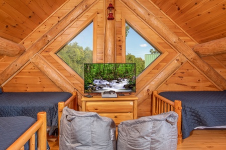 Large windows behind the TV in the bunk room of the game room at Great View Lodge, a 5-bedroom cabin rental located in Pigeon Forge