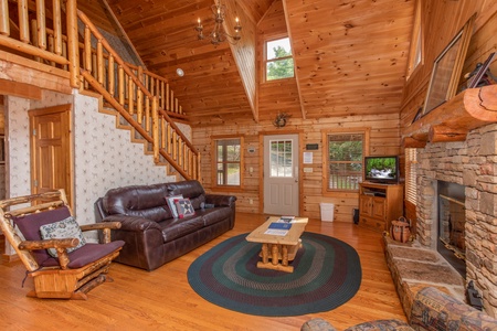Living room with a leather couch, log glider, fireplace, and television at Cabin in the Clouds, a 3-bedroom cabin rental located in Pigeon Forge